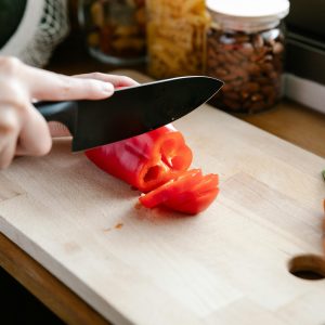 Crop anonymous person slicing ripe fresh red capsicum on chopping board on kitchen counter